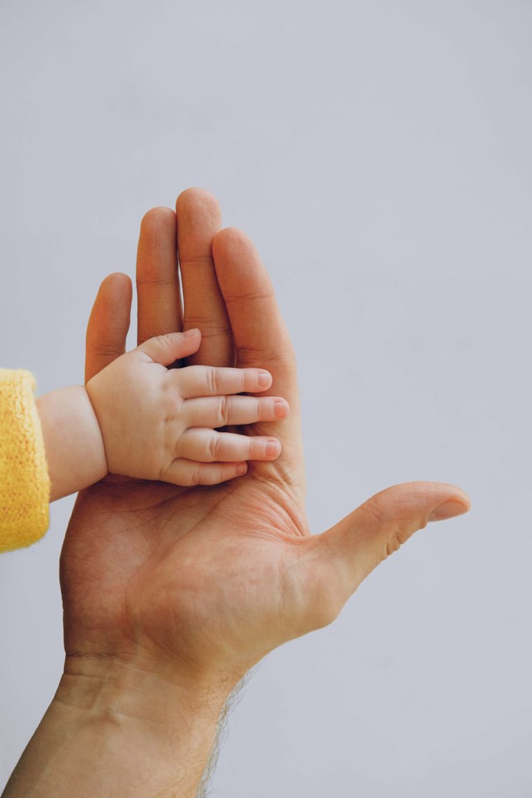 a hand of an adult holding a hand of a newborn