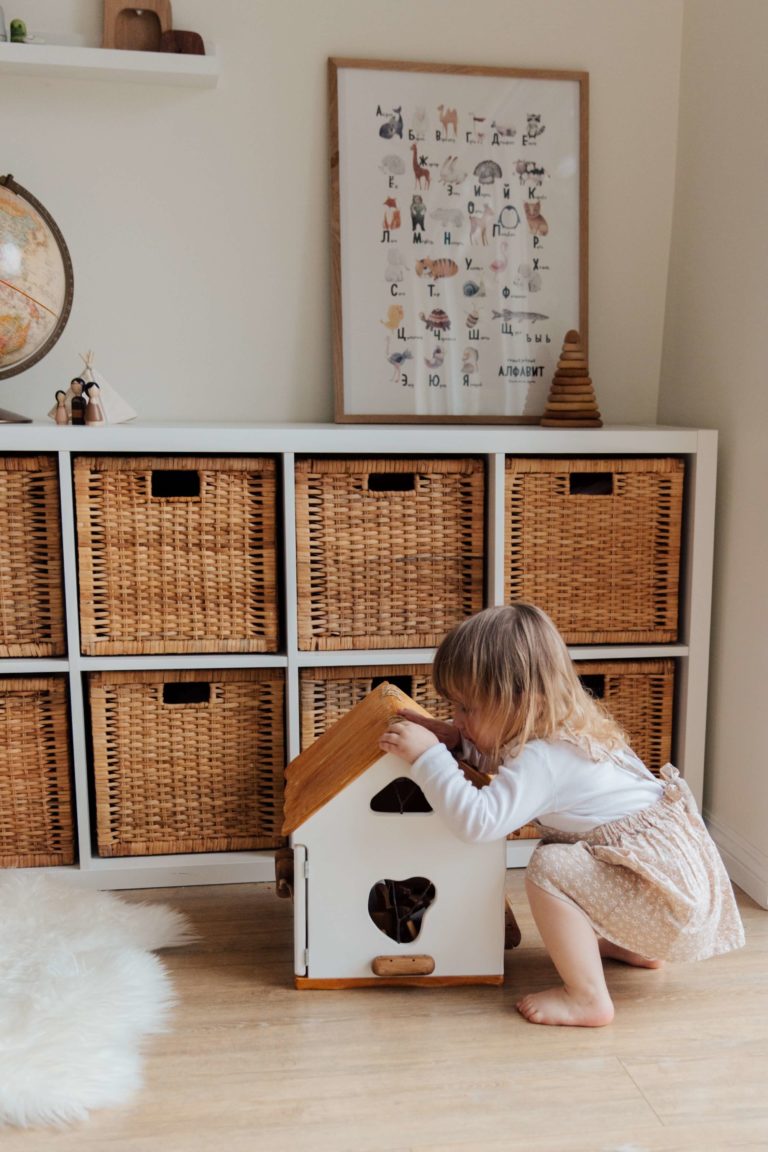 a little girl is playing with a doll house inside a room, clothes organizers are in the back