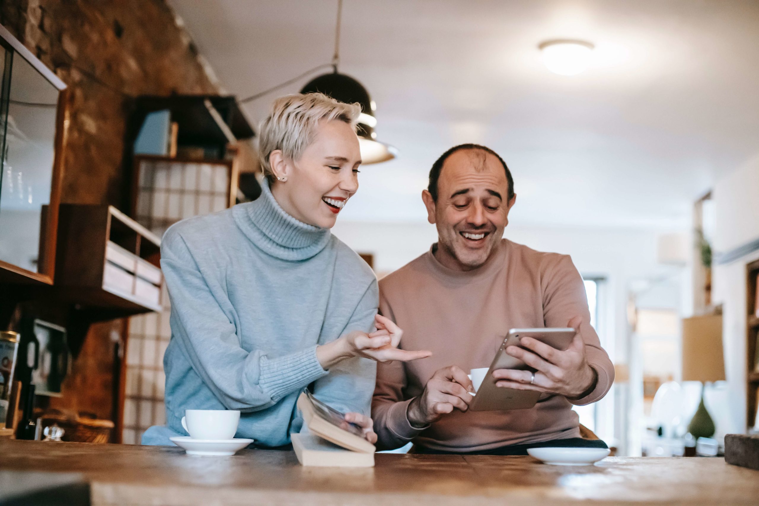 a woman and a man are talking and laughing looking at a tablet